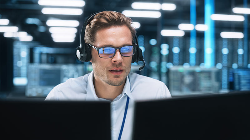 Photo of a man looking at computer screen and and talking on a headset